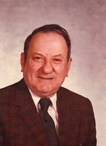 Head and shoulders portrait of Principal George Tankard. He is wearing a dark maroon jacket, white shirt, and dark brown tie. He has a kind smile.