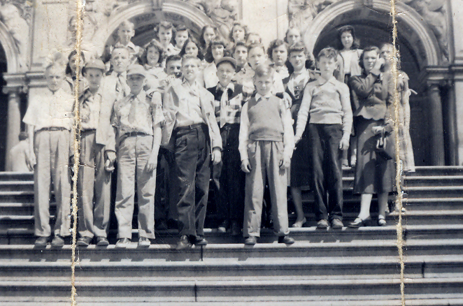 Black and white photograph of Forestville’s seventh grade class during the 1952 to 1953 school year standing on the steps in front of a building in Washington, D.C. 25 students and three adults are visible. The building behind them has decorative arched entryways with tall columns.