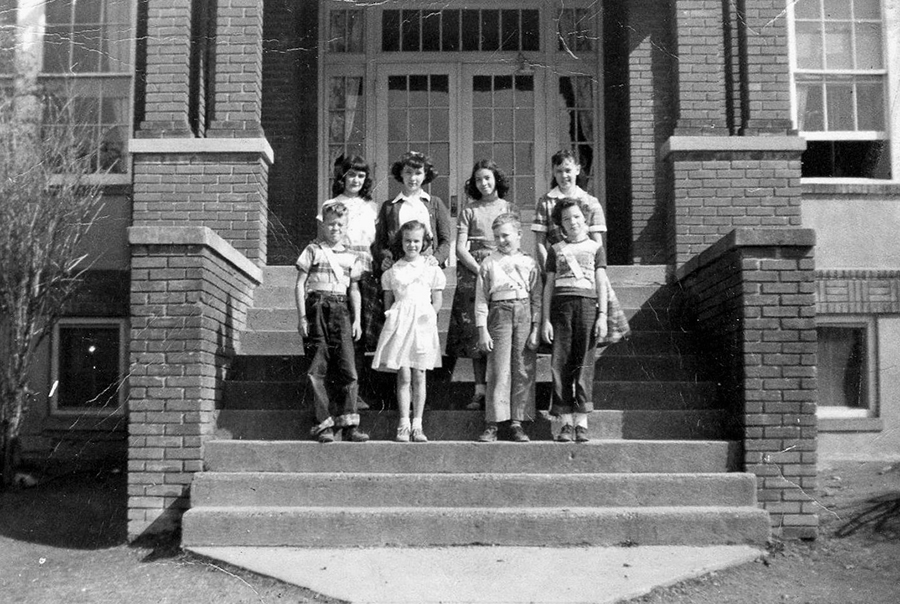 Undated black and white photograph of Forestville Elementary School’s Student Council Association officers, most likely taken during the 1940s. Eight children are pictured, standing in two rows on the steps in front of the main entrance. There are five girls and three boys. The three boys are wearing belts and sashes indicating they are on the school’s Safety Patrol. 