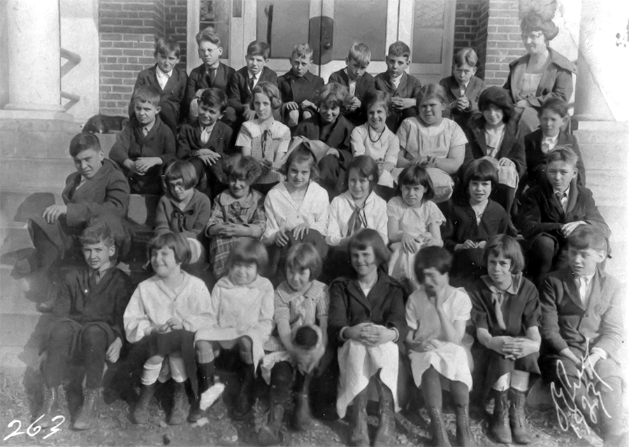 Black and white photograph of students at Forestville Elementary School taken in the 1930s or 1940s. The children and their teacher are posed on the steps in front of the building. 31 children are pictured, 17 girls and 14 boys. A female teacher is seated in the back row on the far right.