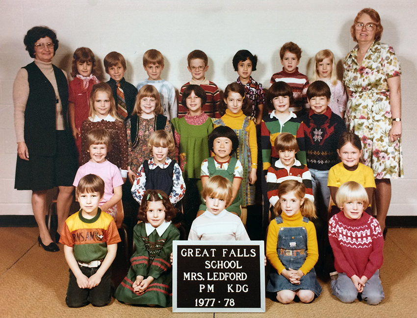 Color photograph from the 1977 to 1978 school year showing Mrs. Ledford’s kindergarten class. 23 children and two adults are pictured. The children are arranged in four rows along the wall in the gymnasium. Two female teachers stand in the back row, one on the right and one on the left.