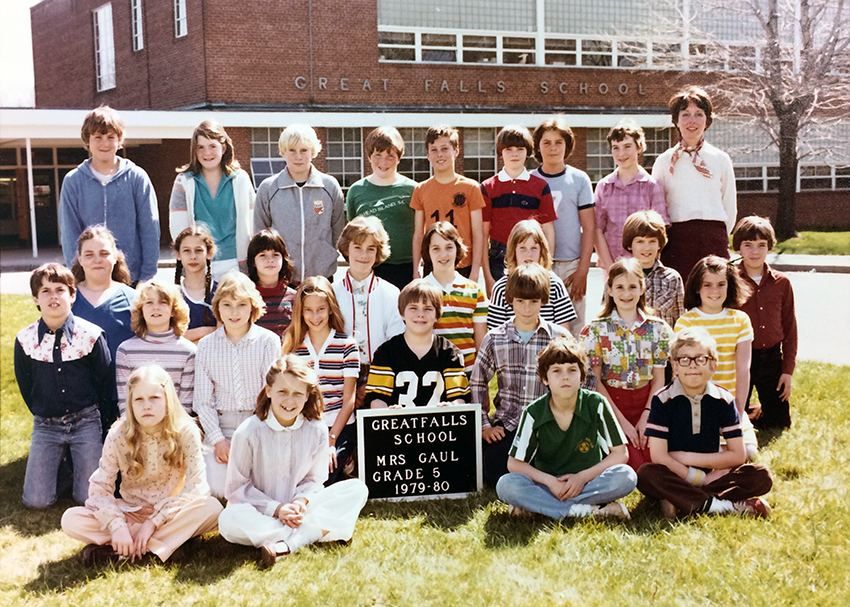 Color photograph from the 1979 to 1980 school year showing Mrs. Gaul’s fifth grade class. 28 children and their teacher are pictured. The children are arranged in four rows on the lawn in front of the school’s main entrance. Mrs. Gaul is standing in the back row on the far right.