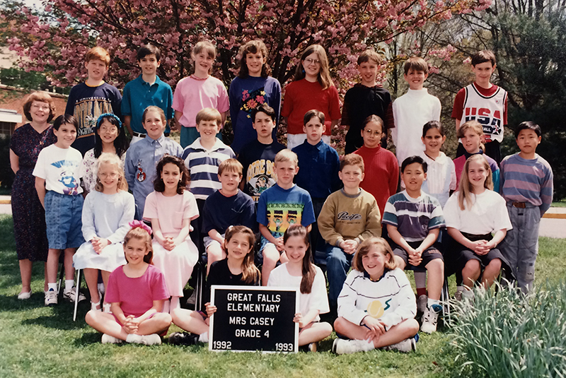 Fourth grade class photograph taken during the 1992 to 1993 school year. 29 students and their teacher are pictured. The children are arranged in four rows, and are posed in front of one of the blooming cherry trees in front of the school. The tree is laden with large pink flowers.