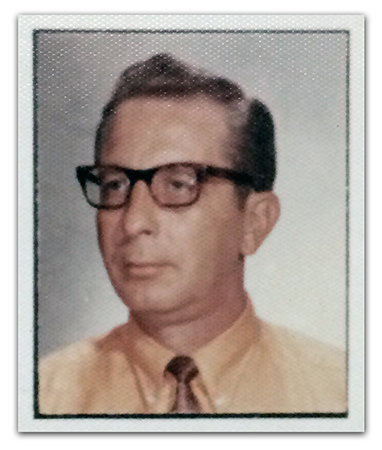 Color head-and-shoulders staff portrait of Principal McClung taken during the 1970 to 1971 school year. He wears glasses, and is wearing a yellow shirt with a brown tie.