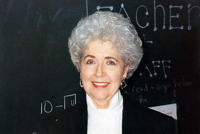Color photograph of Principal Agnes Brown from Great Falls Elementary School’s 1993 to 1994 yearbook. She has short grey hair and is standing in front of a chalkboard. She is wearing a white shirt and a dark jacket.